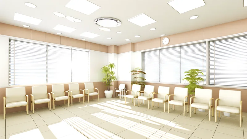 ベージュとクリーム色の椅子が並ぶ明るい産婦人科クリニックの待合室、緑の観葉植物と大きな窓