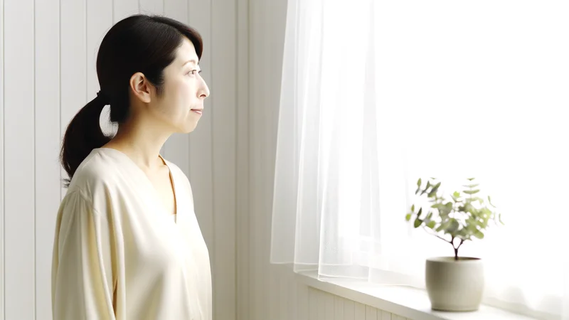 穏やかな表情で窓の外を見つめる女性。卵巣嚢腫と向き合うイメージ