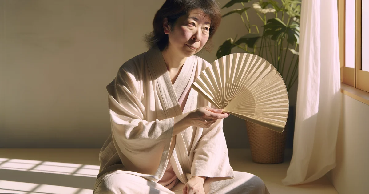 窓際で扇子を手に過ごす日本人女性。ホットフラッシュのほてりを和らげようとしているイメージ