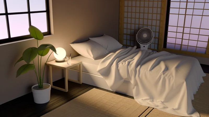扇風機と観葉植物を配した和モダンな寝室のセルフケア環境。白いコットンシーツのベッド、ベッドサイドランプ、窓から差し込む光