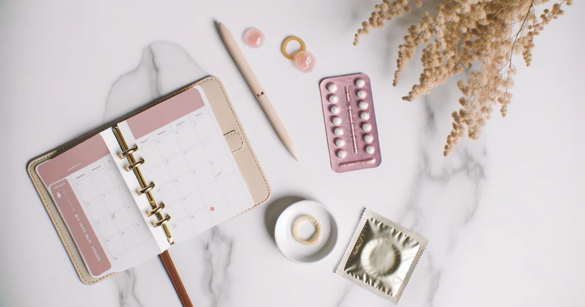 避妊薬のブリスターパックとカレンダー、ドライフラワーを並べたフラットレイ写真