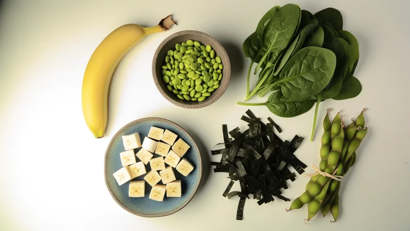 バナナ・枝豆・ほうれん草・わかめ・さや付き豆などアルカリ性食品が白いテーブルに並ぶフラットレイ