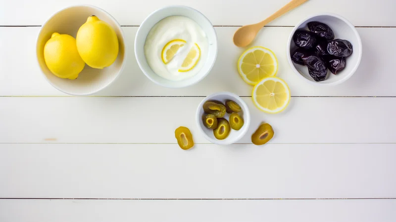 レモン・ヨーグルト・プルーン・オリーブなど酸性食品が白いテーブルに並ぶフラットレイ